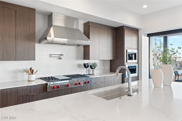 kitchen featuring light stone countertops, sink, wall chimney exhaust hood, stainless steel appliances, and backsplash