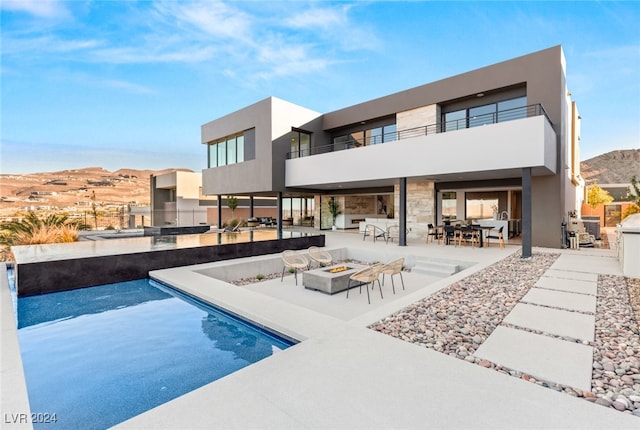 rear view of property featuring a mountain view, a balcony, an outdoor fire pit, and a patio