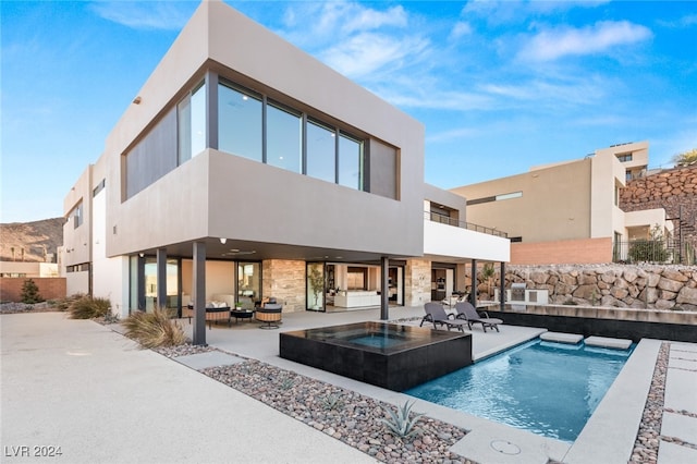 rear view of property featuring pool water feature, a pool with hot tub, an outdoor hangout area, and a patio