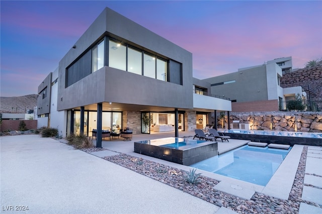 back house at dusk featuring a swimming pool with hot tub and a patio