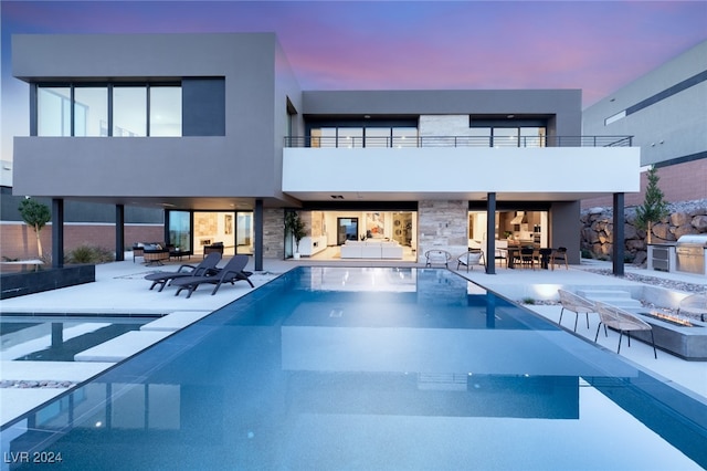 back house at dusk featuring a patio, a balcony, and an indoor pool