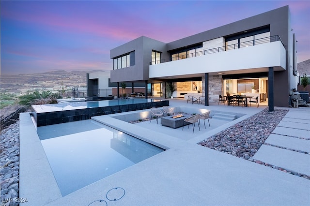 back house at dusk with a fire pit, a balcony, and a patio