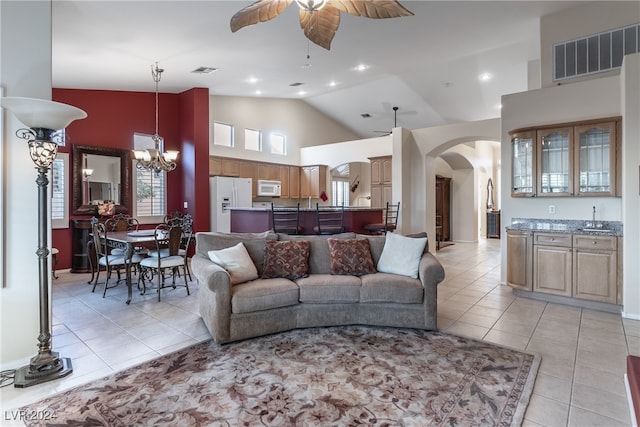 tiled living room featuring high vaulted ceiling and ceiling fan with notable chandelier