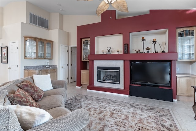 living room with ceiling fan, sink, light tile patterned floors, lofted ceiling, and a tiled fireplace