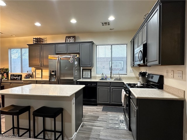 kitchen featuring light stone counters, sink, black appliances, a center island, and light hardwood / wood-style floors