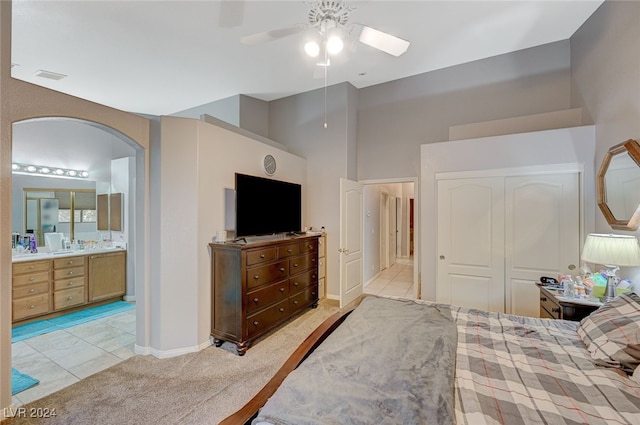 bedroom with light tile patterned floors, a closet, ensuite bath, and ceiling fan