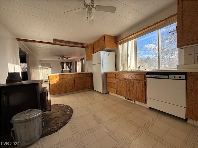 kitchen featuring white appliances, a wood stove, sink, ceiling fan, and kitchen peninsula