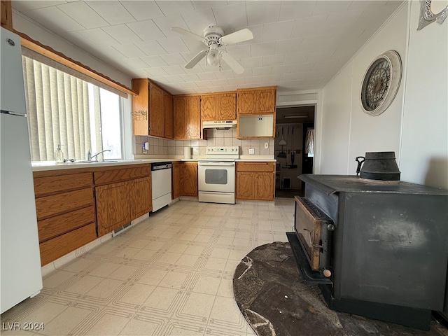 kitchen featuring a wood stove, ceiling fan, sink, tasteful backsplash, and white appliances