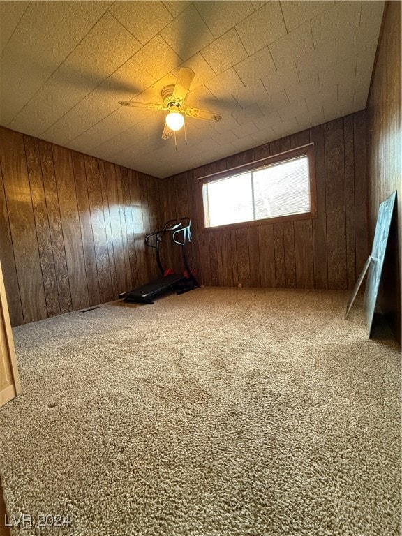 empty room featuring ceiling fan, wooden walls, and carpet floors