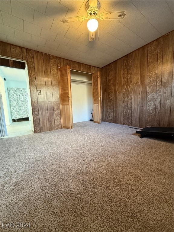 unfurnished room featuring carpet flooring, ceiling fan, and wooden walls