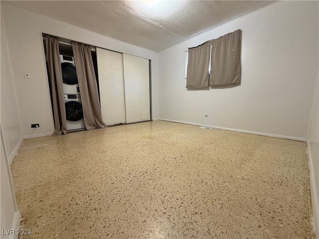 unfurnished bedroom with a textured ceiling, a closet, and stacked washer and clothes dryer