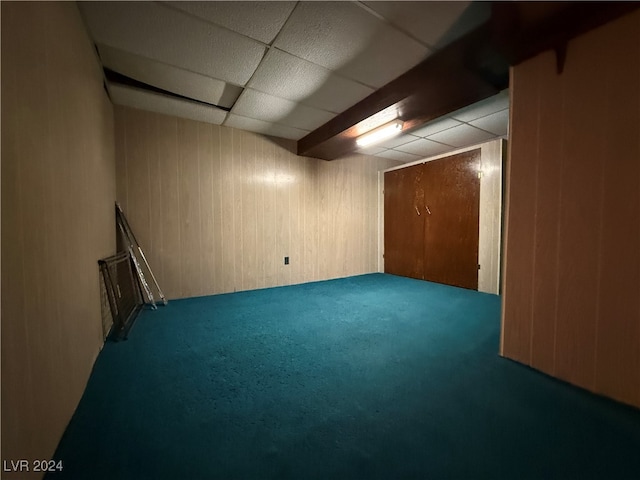 basement with a drop ceiling, wood walls, and carpet floors