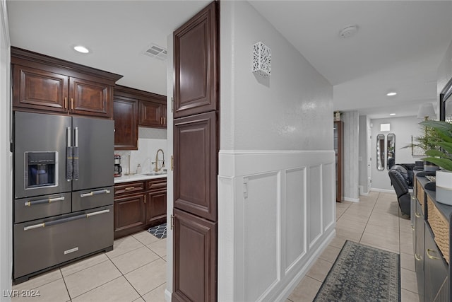 kitchen featuring dark brown cabinets, high end fridge, light tile patterned flooring, and sink