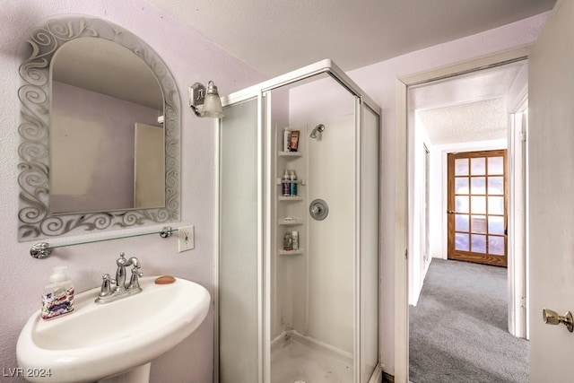 bathroom with a textured ceiling, a shower with shower door, and sink