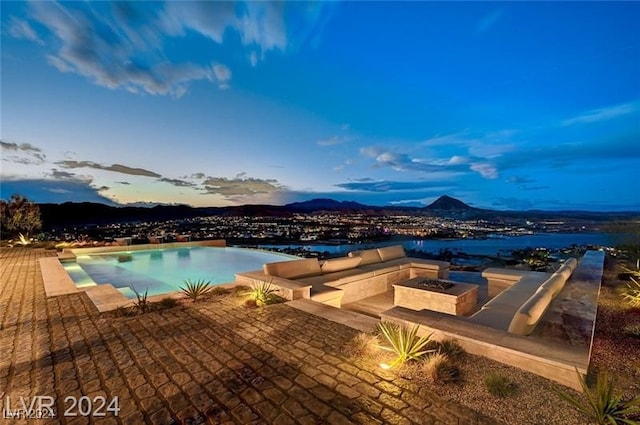 pool at dusk with a mountain view, an outdoor fire pit, and a patio area