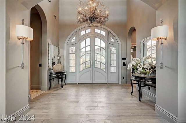 foyer entrance featuring a towering ceiling, light wood-type flooring, and a notable chandelier