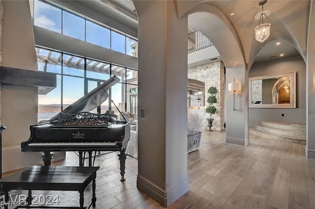 miscellaneous room with a towering ceiling, light hardwood / wood-style flooring, and a notable chandelier