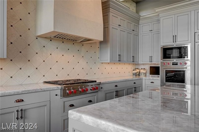 kitchen featuring tasteful backsplash, light stone counters, exhaust hood, and stainless steel gas stovetop