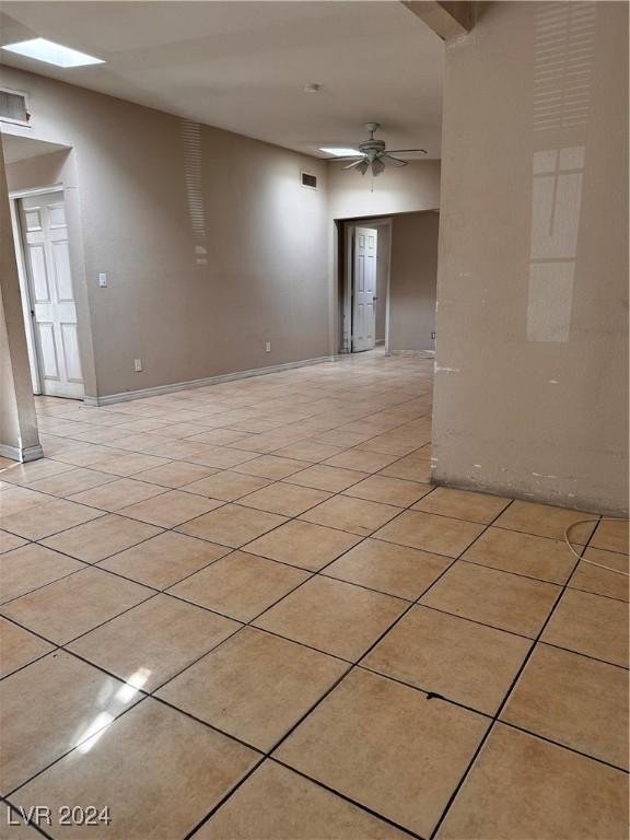 tiled empty room featuring ceiling fan and a skylight