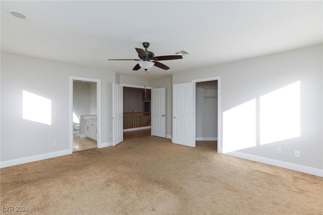 unfurnished bedroom with light carpet, a spacious closet, ceiling fan, and ensuite bathroom