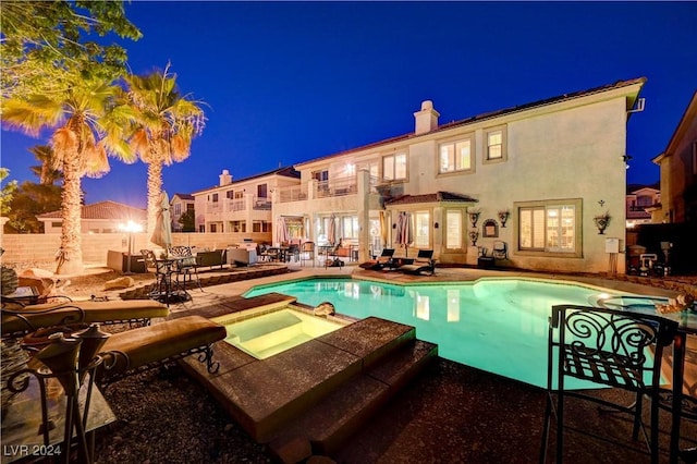 pool at night featuring a patio area and an in ground hot tub