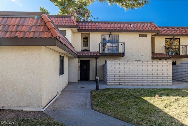 exterior space with a balcony, a yard, a tiled roof, and stucco siding