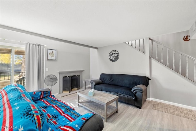 living room featuring stairs, a fireplace with raised hearth, light wood finished floors, and baseboards