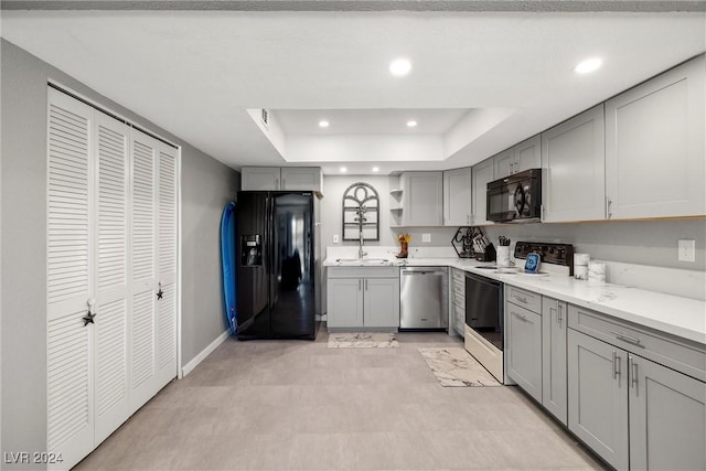 kitchen featuring a tray ceiling, recessed lighting, gray cabinets, light countertops, and black appliances