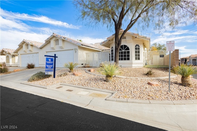 view of front facade with stucco siding, concrete driveway, an attached garage, a gate, and fence