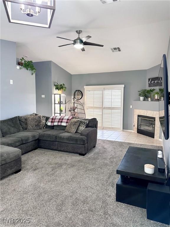 carpeted living area with a ceiling fan, visible vents, vaulted ceiling, and a tiled fireplace