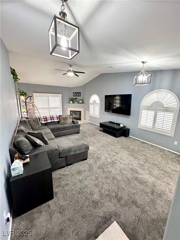 living room with carpet floors, a ceiling fan, vaulted ceiling, a tile fireplace, and plenty of natural light