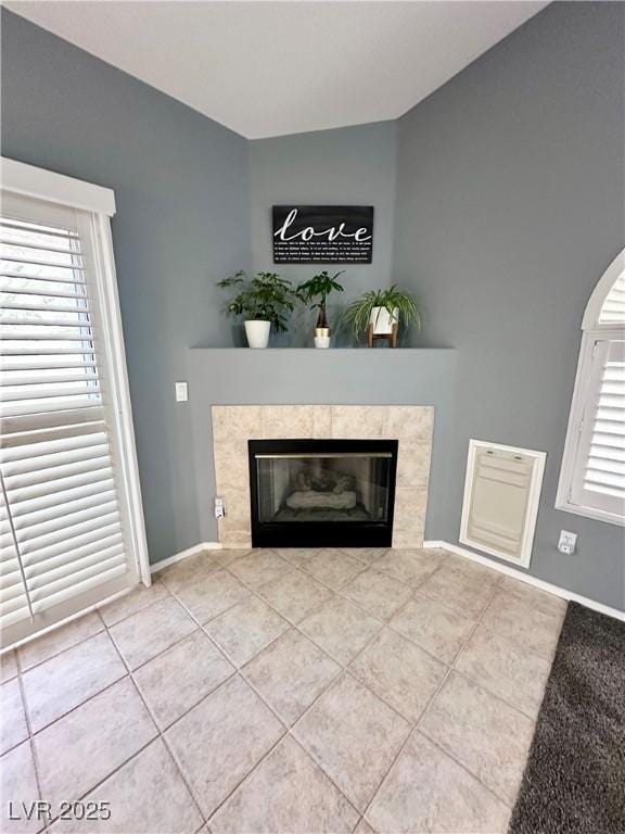 unfurnished living room featuring a tile fireplace, tile patterned flooring, lofted ceiling, and baseboards