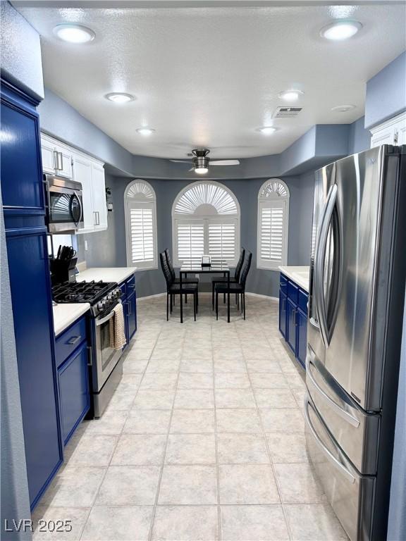 kitchen with stainless steel appliances, light countertops, blue cabinets, and ceiling fan