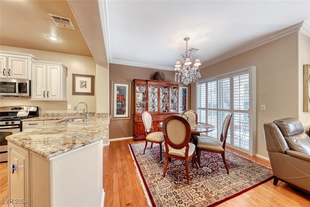 dining area featuring ornamental molding, light wood-type flooring, a notable chandelier, and sink