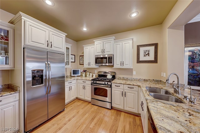 kitchen with appliances with stainless steel finishes, light wood-type flooring, light stone counters, sink, and white cabinets