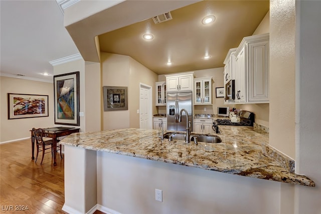 kitchen featuring kitchen peninsula, appliances with stainless steel finishes, sink, light hardwood / wood-style flooring, and white cabinets