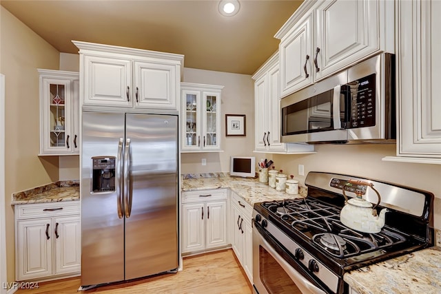 kitchen with white cabinets, stainless steel appliances, light hardwood / wood-style flooring, and light stone countertops