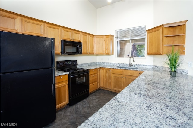 kitchen featuring black appliances, light stone countertops, sink, and a towering ceiling