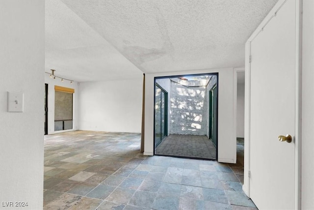 empty room with track lighting, stone finish floor, and a textured ceiling