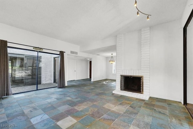 unfurnished living room with a textured ceiling, a fireplace, visible vents, baseboards, and stone finish flooring