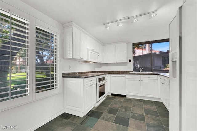 kitchen featuring dark countertops, stone finish flooring, white cabinets, a sink, and white appliances