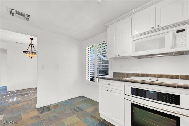 kitchen with white appliances, visible vents, white cabinetry, stone finish floor, and dark countertops