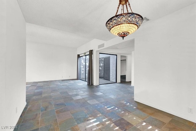 empty room with stone finish flooring, visible vents, a textured ceiling, and baseboards