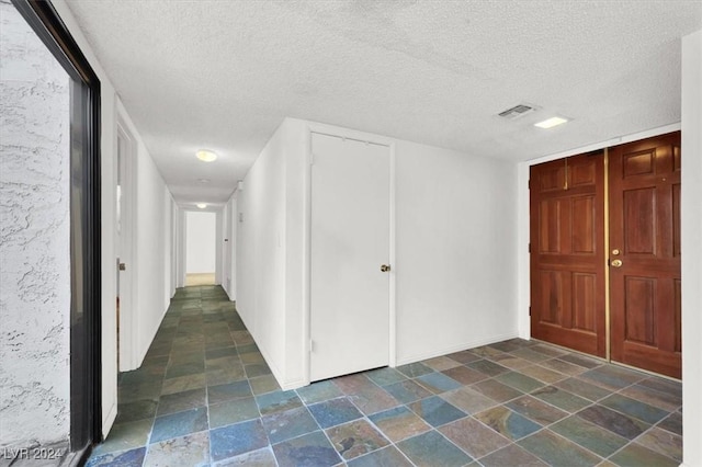 hallway with a textured ceiling, stone finish floor, and visible vents