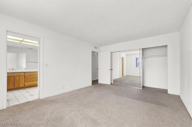 unfurnished bedroom featuring a closet, a textured ceiling, connected bathroom, and light colored carpet