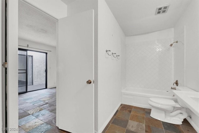 bathroom featuring baseboards, visible vents, bathing tub / shower combination, toilet, and stone tile flooring