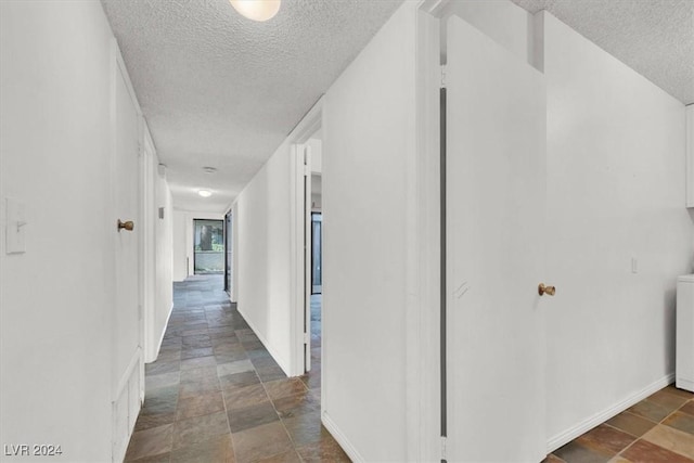 hall featuring baseboards, stone finish floor, and a textured ceiling