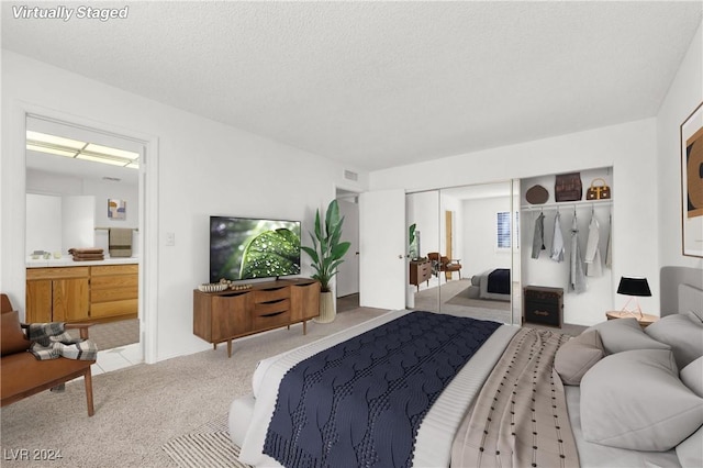 bedroom featuring light carpet, a textured ceiling, a closet, and ensuite bathroom