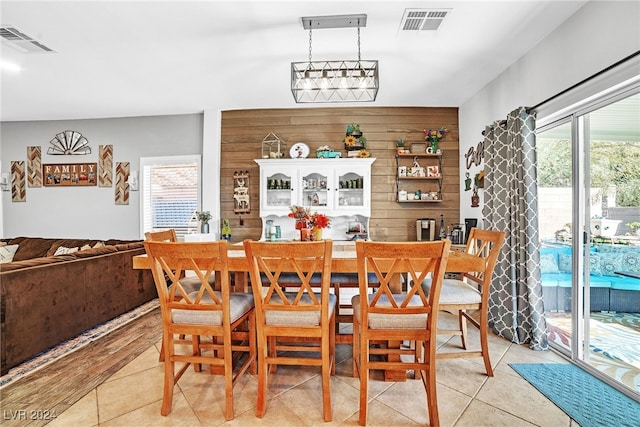 tiled dining room featuring wooden walls, a wealth of natural light, and a chandelier