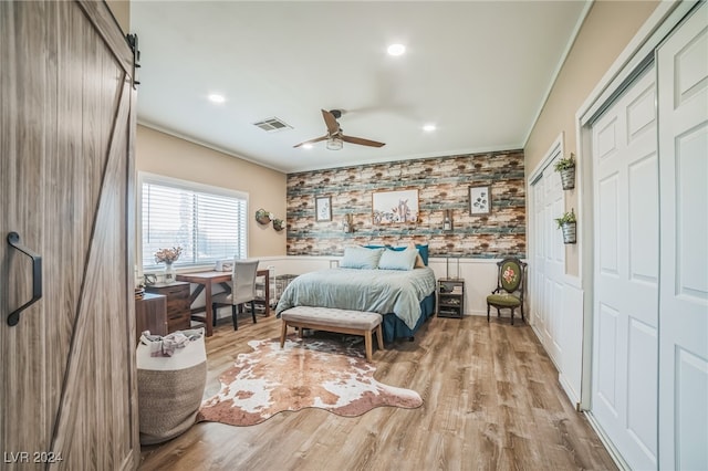 bedroom with ceiling fan, a barn door, ornamental molding, and light hardwood / wood-style flooring